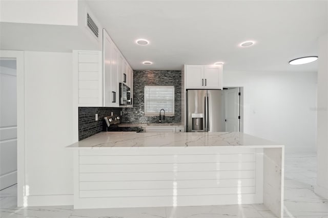 kitchen with a peninsula, marble finish floor, light stone countertops, stainless steel appliances, and a sink