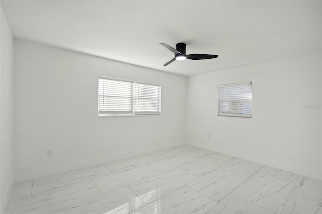 empty room with marble finish floor, a ceiling fan, and baseboards
