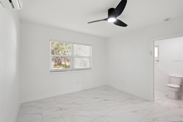 empty room with a wall unit AC, marble finish floor, baseboards, and a ceiling fan