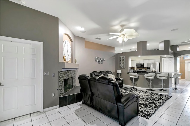 living room featuring visible vents, ceiling fan, a tiled fireplace, and light tile patterned floors