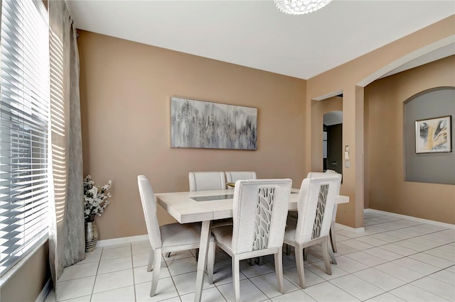 dining space with light tile patterned floors, baseboards, arched walkways, and a healthy amount of sunlight