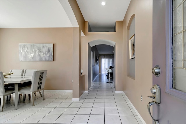 foyer with arched walkways, light tile patterned flooring, and baseboards