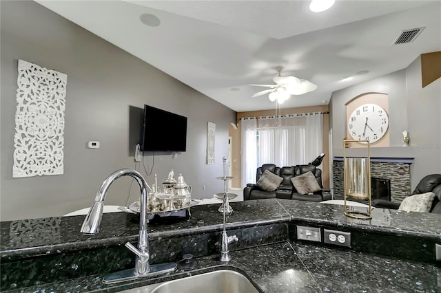 kitchen featuring visible vents, a ceiling fan, open floor plan, a sink, and a stone fireplace