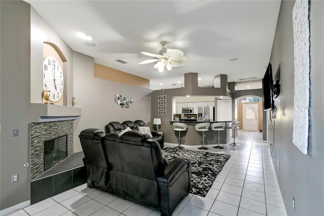 living area with light tile patterned floors, visible vents, ceiling fan, a tile fireplace, and baseboards