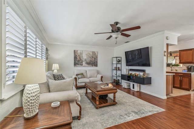 living area featuring wood finished floors, visible vents, a ceiling fan, baseboards, and ornamental molding