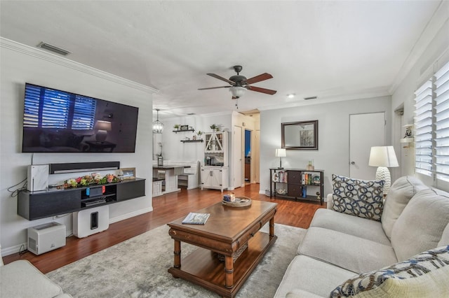 living room with a ceiling fan, wood finished floors, visible vents, and ornamental molding