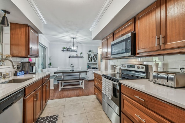 kitchen with brown cabinets, ornamental molding, a sink, appliances with stainless steel finishes, and light tile patterned floors