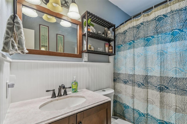 bathroom featuring vanity, a shower with shower curtain, toilet, and wainscoting