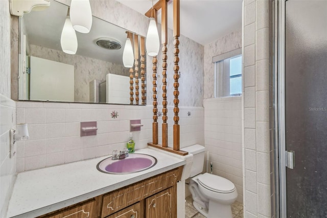 full bath with wallpapered walls, toilet, vanity, wainscoting, and tile walls