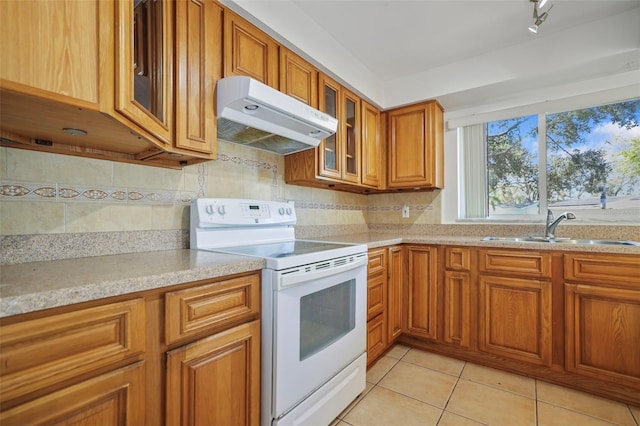 1549 San Christopher Dr, Dunedin, FL 34698 - kitchen with under cabinet range hood, a sink, brown cabinets, tasteful backsplash, and white electric range oven