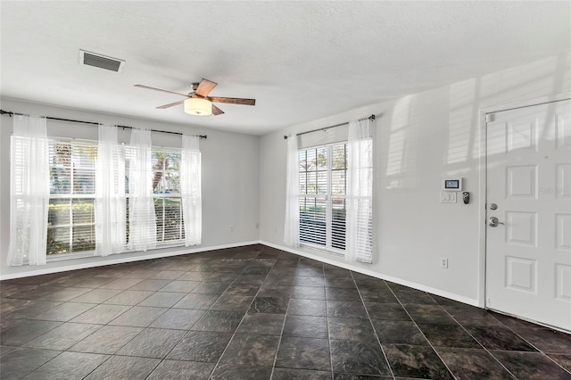 unfurnished room with a textured ceiling, a ceiling fan, visible vents, and baseboards