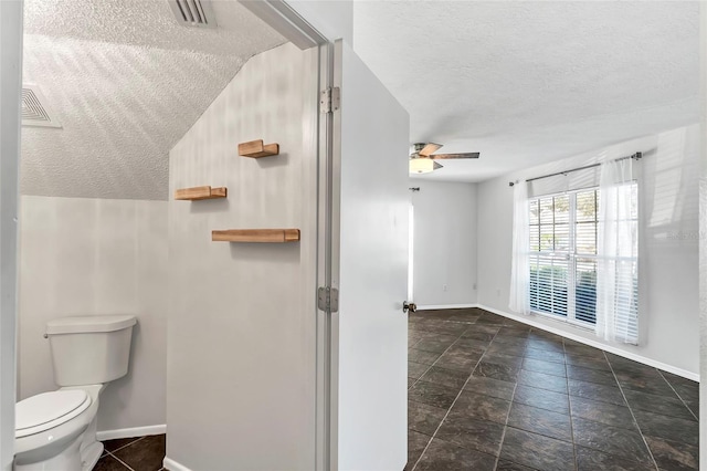 bathroom featuring visible vents, toilet, a ceiling fan, a textured ceiling, and baseboards