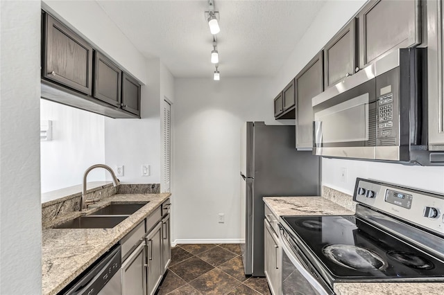 kitchen with a textured ceiling, light stone counters, a sink, baseboards, and appliances with stainless steel finishes