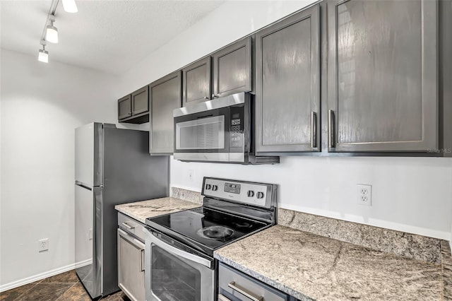 kitchen featuring a textured ceiling, stainless steel appliances, light stone counters, and baseboards