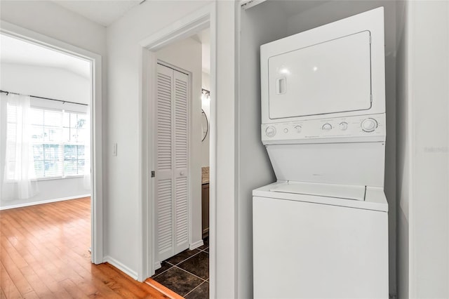 laundry area featuring stacked washer and dryer, wood finished floors, laundry area, and baseboards