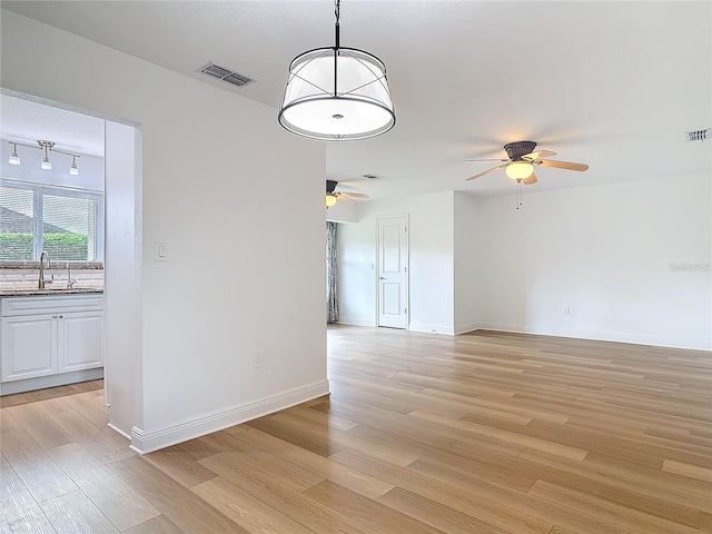 empty room featuring light wood finished floors, visible vents, a sink, ceiling fan, and baseboards