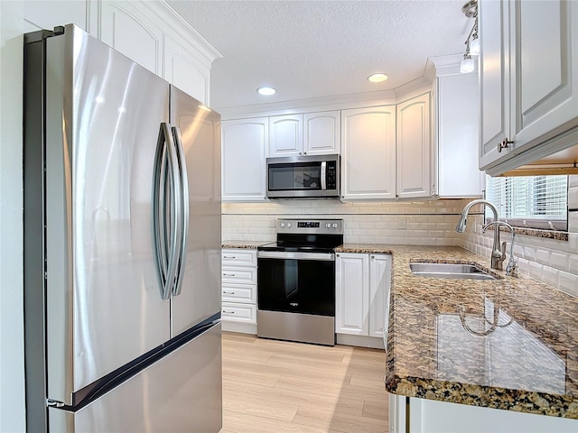 kitchen featuring stainless steel appliances, tasteful backsplash, white cabinets, a sink, and dark stone counters