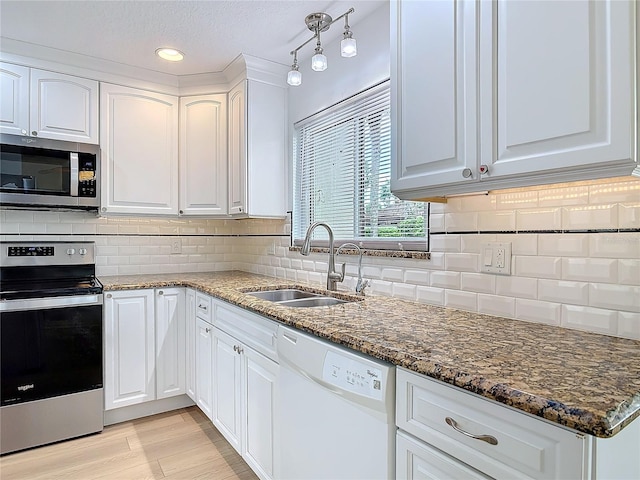 kitchen featuring appliances with stainless steel finishes, white cabinets, a sink, and dark stone countertops