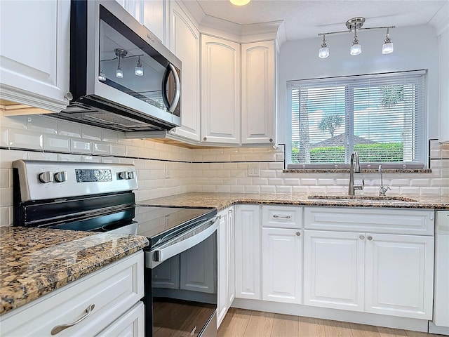 kitchen with stone countertops, stainless steel appliances, a sink, white cabinetry, and decorative backsplash