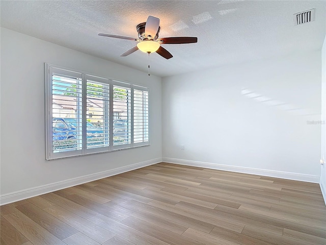 spare room with light wood-type flooring, visible vents, a textured ceiling, and baseboards