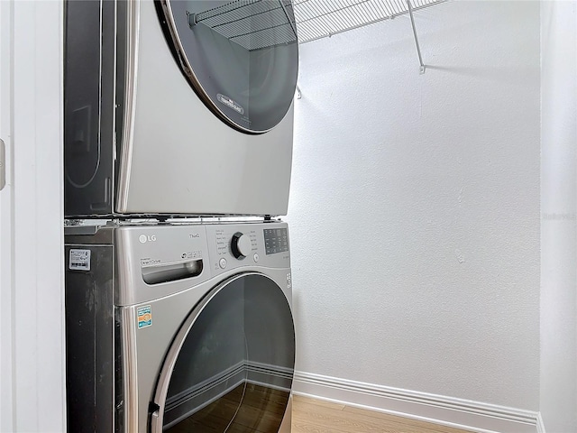 clothes washing area with a textured wall, laundry area, wood finished floors, baseboards, and stacked washing maching and dryer