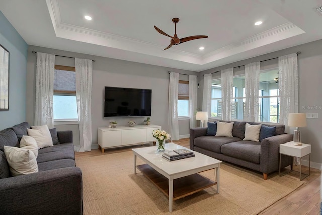 living area with light wood finished floors, a tray ceiling, ornamental molding, and a ceiling fan