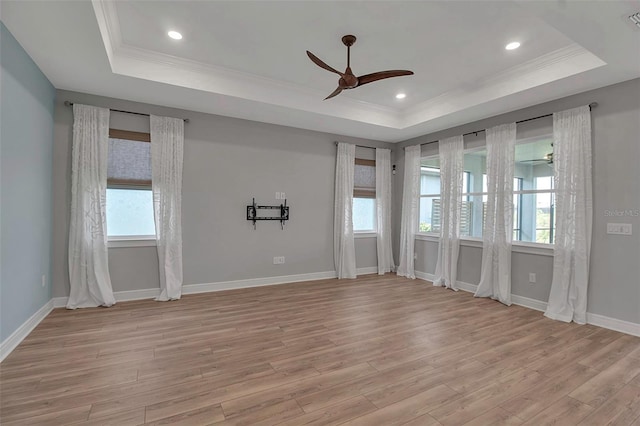 spare room featuring a raised ceiling, a ceiling fan, ornamental molding, light wood-type flooring, and baseboards