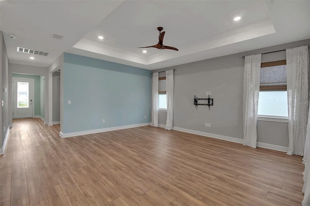 spare room with visible vents, a ceiling fan, light wood-style flooring, a tray ceiling, and crown molding