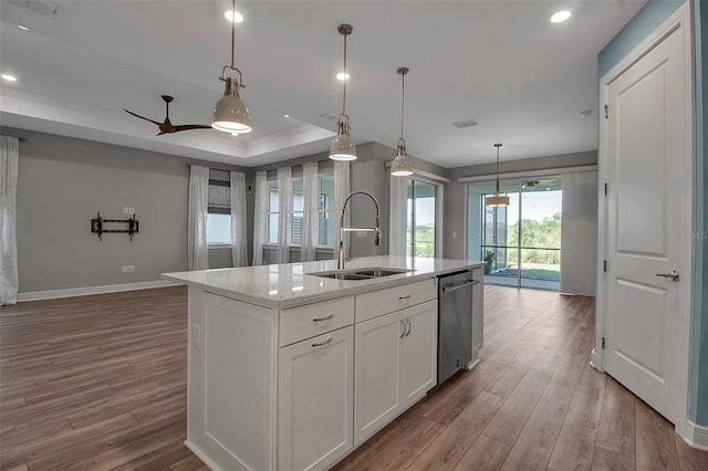 kitchen featuring wood finished floors, a sink, white cabinets, stainless steel dishwasher, and a center island with sink