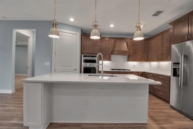 kitchen with custom range hood, backsplash, appliances with stainless steel finishes, a sink, and wood finished floors