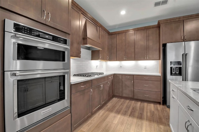 kitchen featuring stainless steel appliances, visible vents, light wood-type flooring, decorative backsplash, and custom range hood