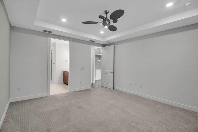 unfurnished bedroom with recessed lighting, light carpet, baseboards, a raised ceiling, and ensuite bath