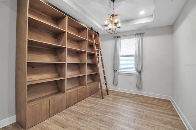 interior space with a chandelier, a raised ceiling, light wood-style flooring, and baseboards