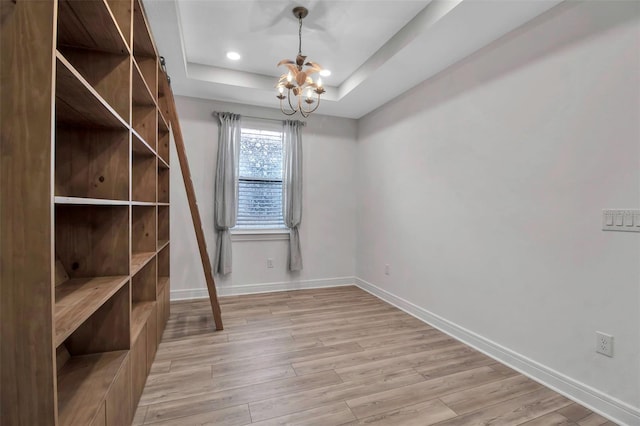 interior space featuring recessed lighting, a raised ceiling, light wood-style flooring, an inviting chandelier, and baseboards