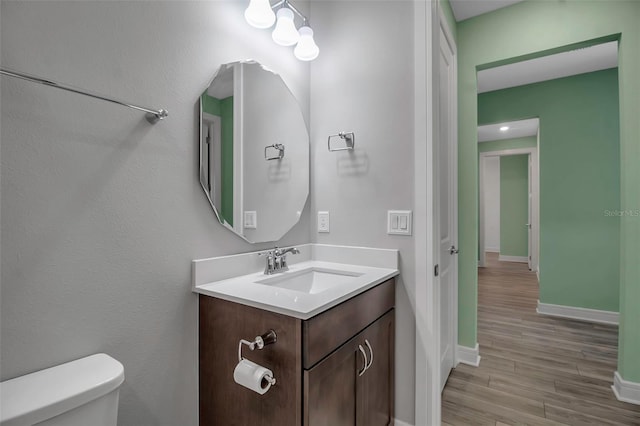 bathroom featuring toilet, baseboards, wood finished floors, and vanity