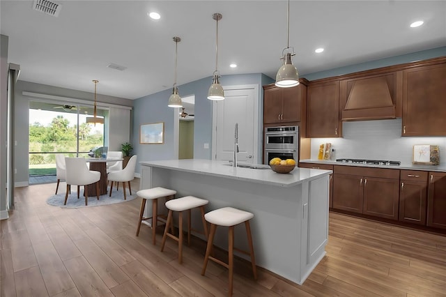 kitchen featuring a sink, appliances with stainless steel finishes, custom exhaust hood, and light wood-style flooring