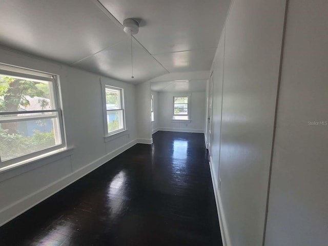 spare room featuring vaulted ceiling, dark wood-style flooring, and baseboards