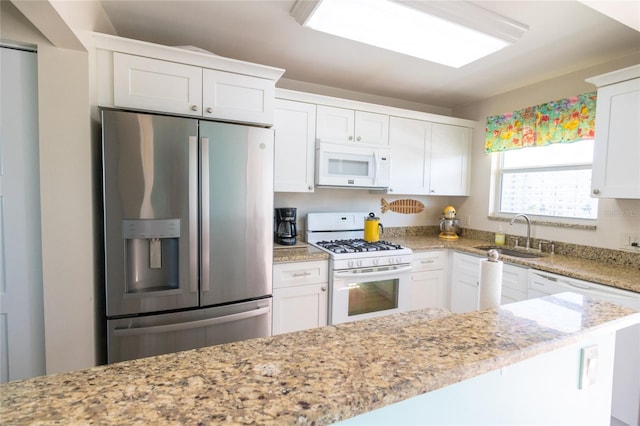 kitchen with white appliances, a sink, white cabinetry, and light stone countertops