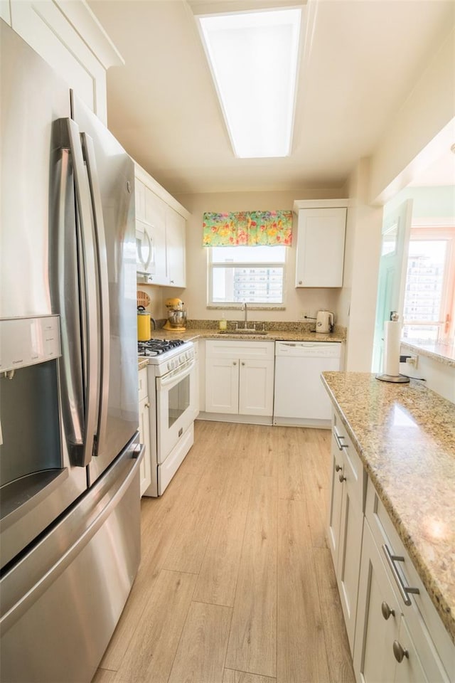 kitchen featuring white appliances, a sink, white cabinetry, light stone countertops, and light wood finished floors