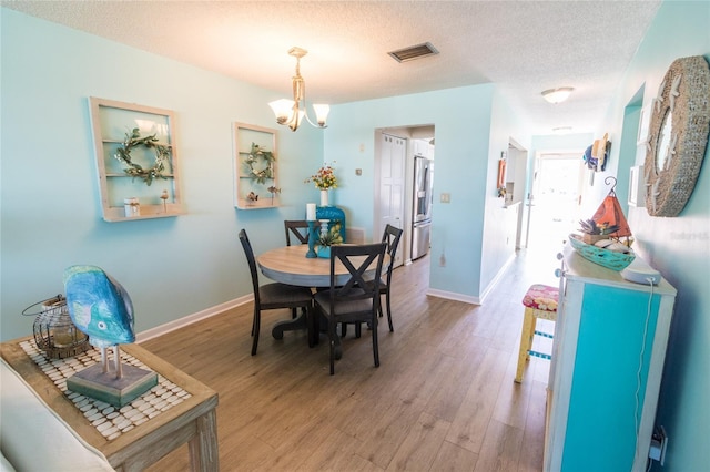 dining space with a textured ceiling, wood finished floors, visible vents, and baseboards