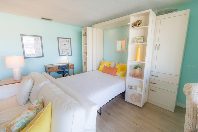 bedroom with visible vents, a textured ceiling, and wood finished floors