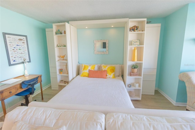 bedroom with a textured ceiling, wood finished floors, and baseboards