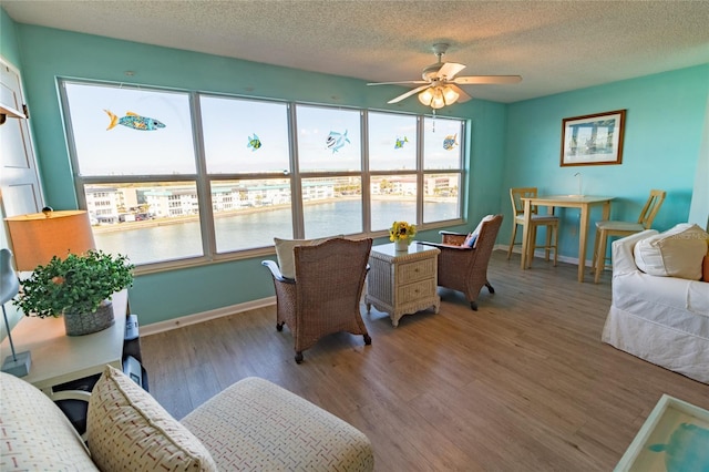 interior space with ceiling fan, a textured ceiling, baseboards, and wood finished floors