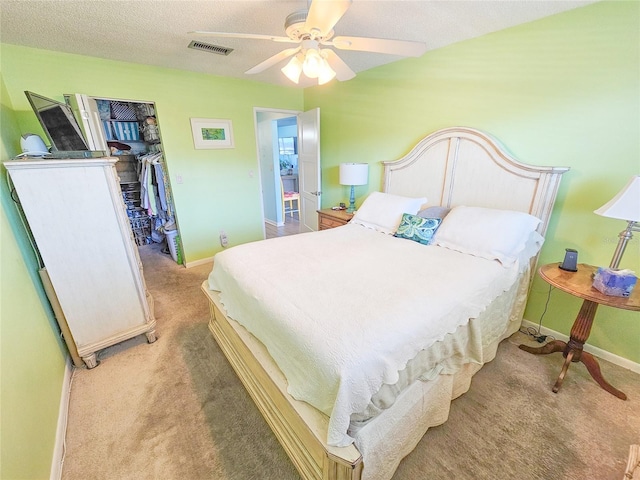 bedroom with ceiling fan, a textured ceiling, light carpet, visible vents, and baseboards