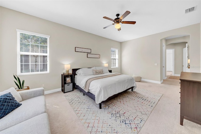 bedroom with light carpet, visible vents, baseboards, and arched walkways