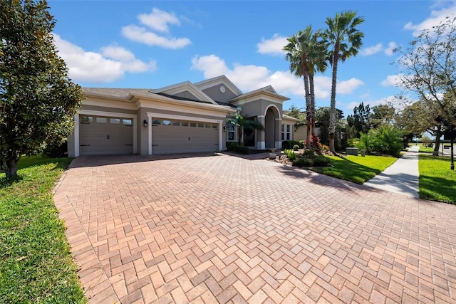 view of front of house featuring a garage, decorative driveway, a front lawn, and stucco siding