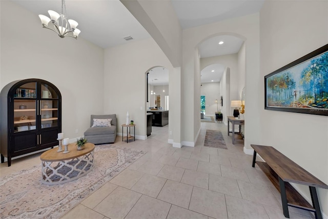 living area with arched walkways, a notable chandelier, light tile patterned floors, visible vents, and baseboards