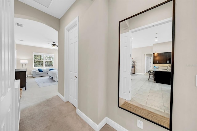 hall with light carpet, visible vents, arched walkways, baseboards, and a sink