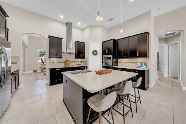 kitchen featuring arched walkways, wall chimney exhaust hood, appliances with stainless steel finishes, and a sink