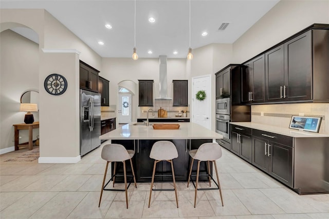 kitchen featuring light countertops, visible vents, appliances with stainless steel finishes, a kitchen island with sink, and wall chimney exhaust hood